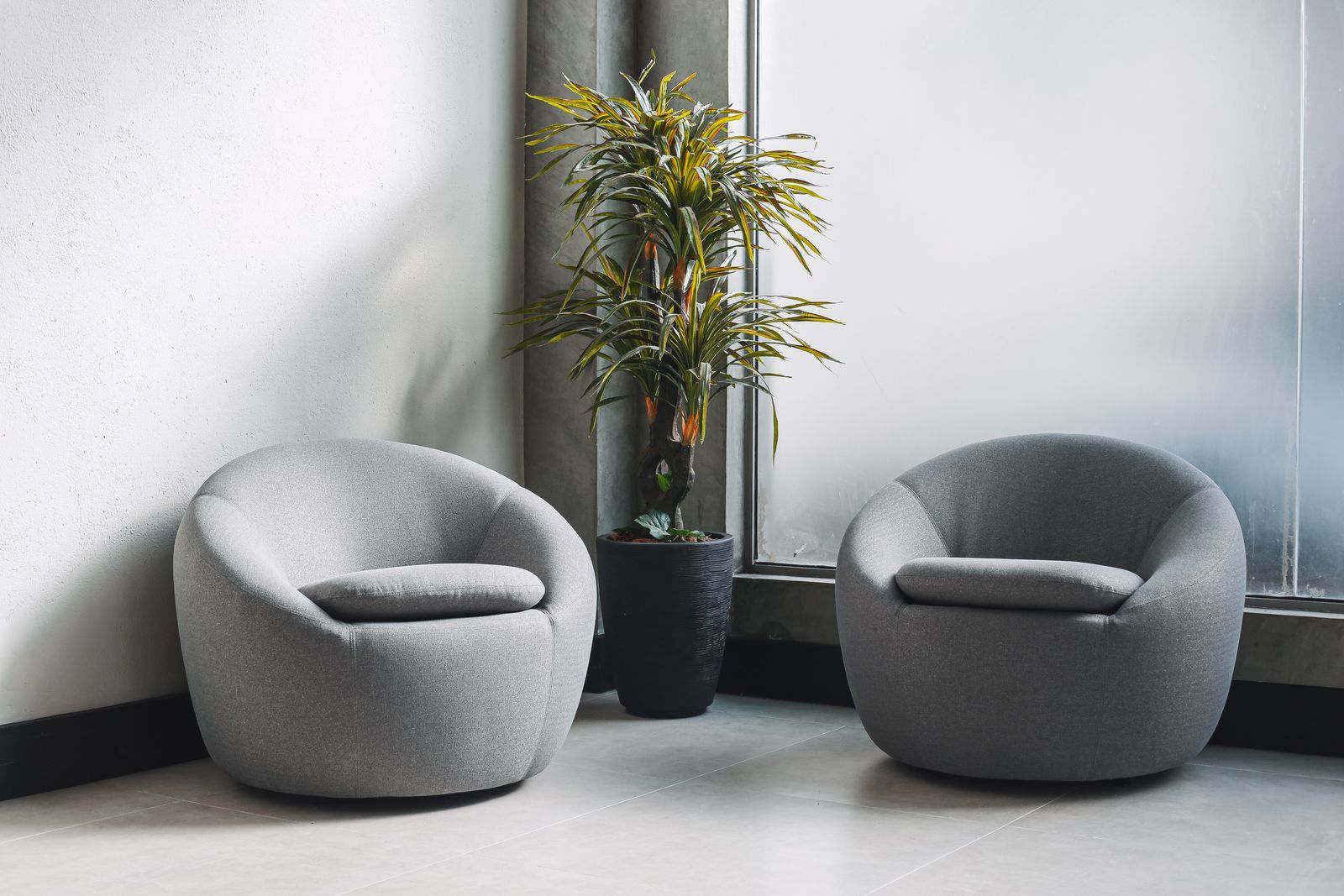 Two grey armchairs with a plant between them in a quiet room.