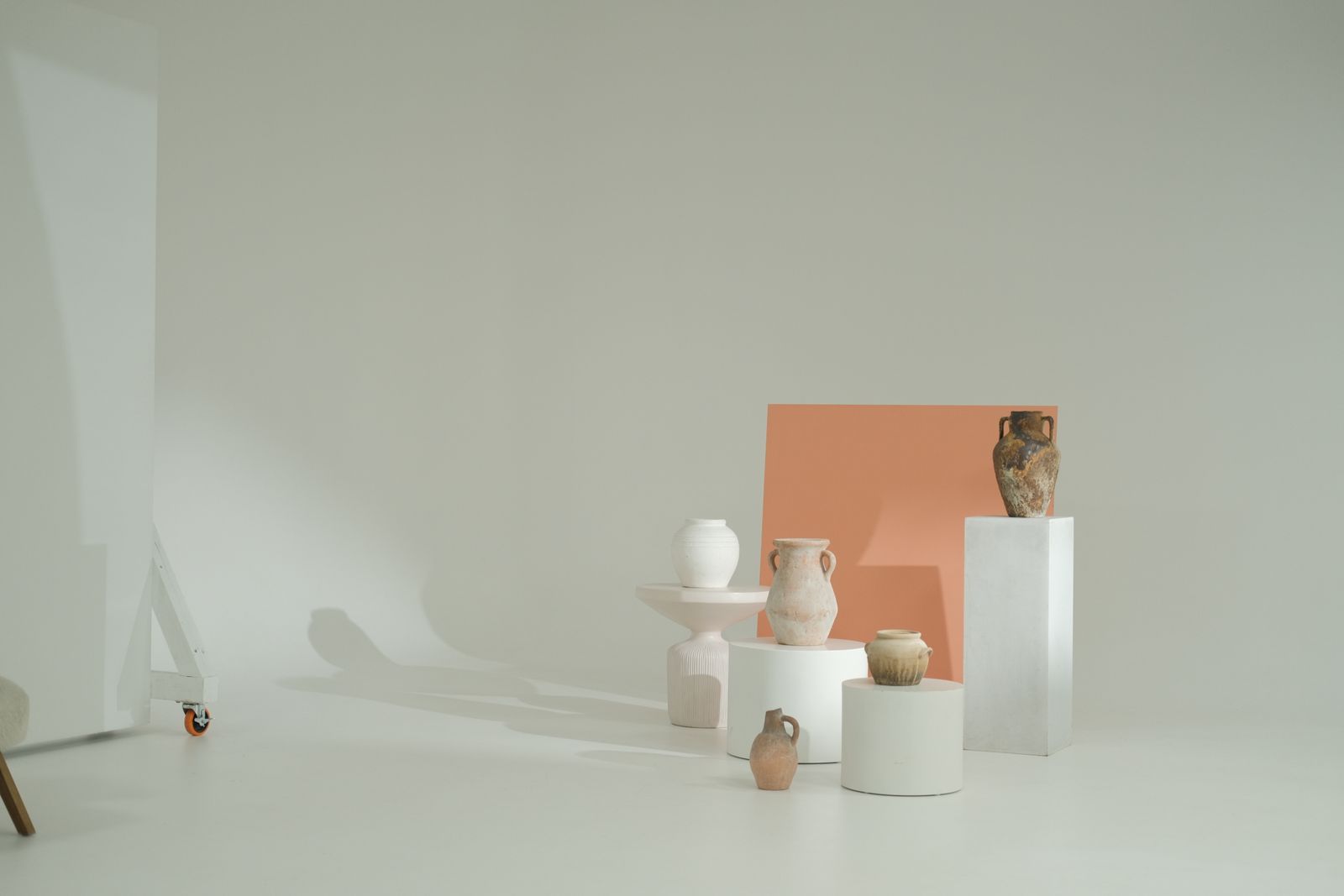 Minimal pottery displayed on white plinths with a muted terracotta backdrop.